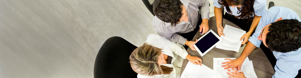 Four people sitting at a office table and reading documents