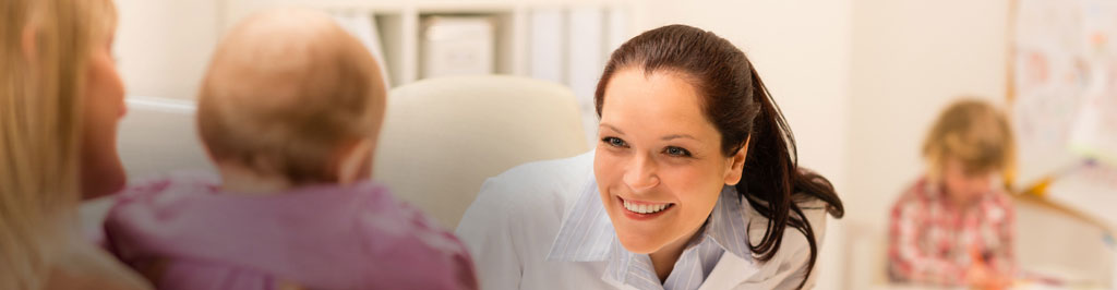 A doctor smiling at a baby in its mother’s lap